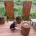 Gas fireplace Sakuru on a wooden deck with rust panels, planters, and a man tending the fire pit.
